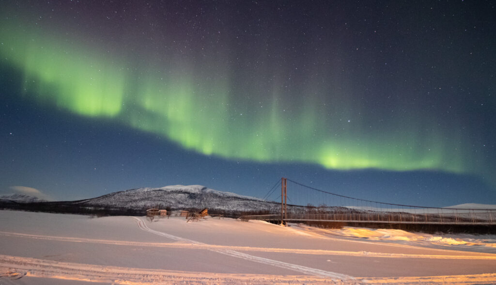 Nordlichter (grün leuchtend) über einem zugefrorenen See an der Grenze zwischen Finnland und Schweden.
